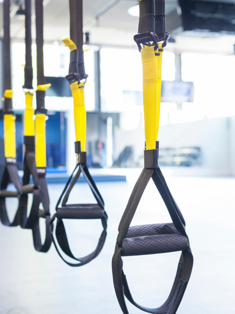 TRX Straps for suspension training hanging from a bar in a gym. 
